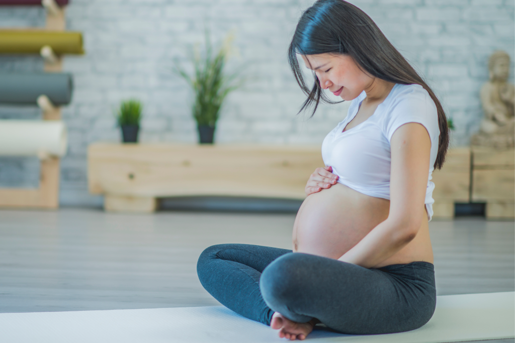 Mujer embarazada sentada con las manos sobre el abdomen.